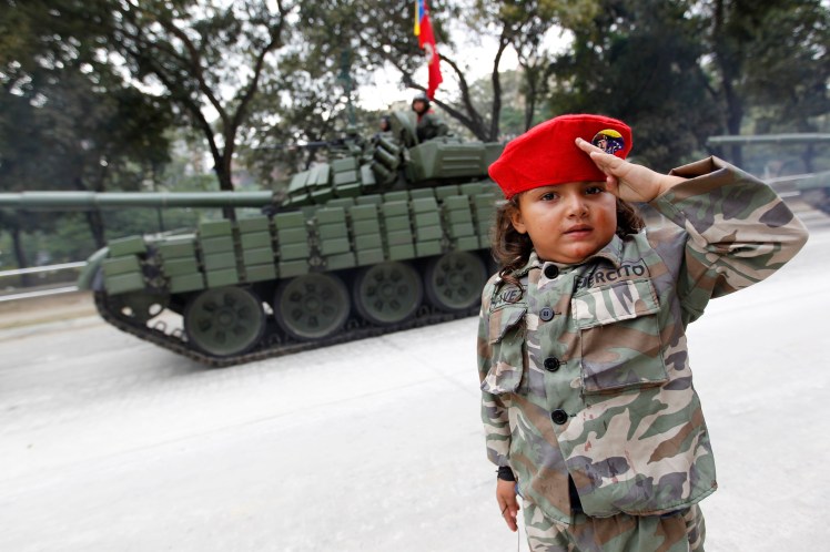 A girls poses next to a tank after the military parade to commemorate the 20th anniversary Venezuelan President Hugo Chavez's failed coup attempt in Caracas