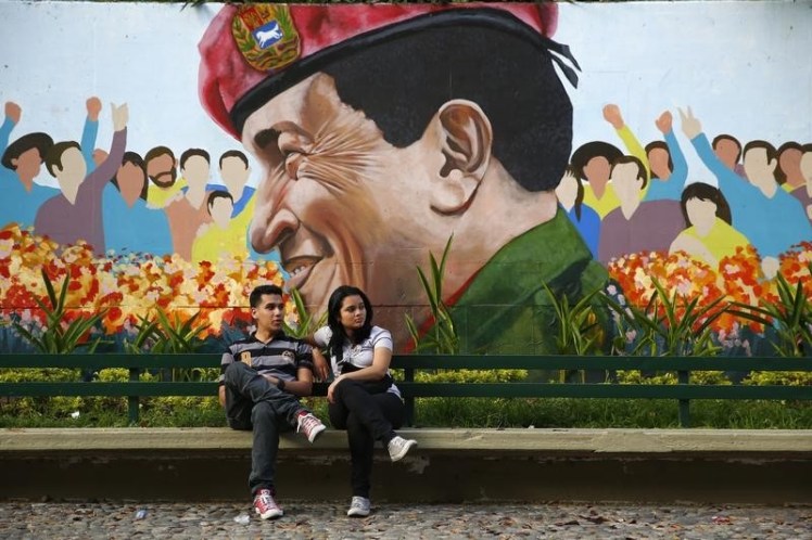 Una pareja se sienta frente a un mural del fallecido líder socialista de Venezuela, Hugo Chávez en Caracas